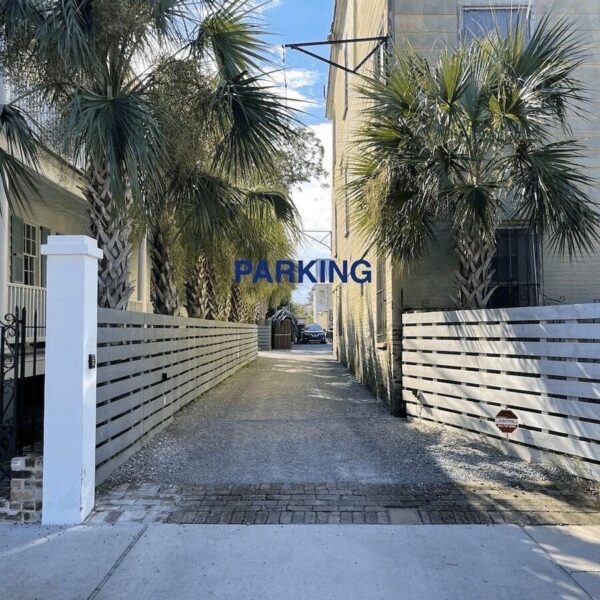 Narrow alleyway with gravel path, palm trees, white fences, and a PARKING sign overhead.