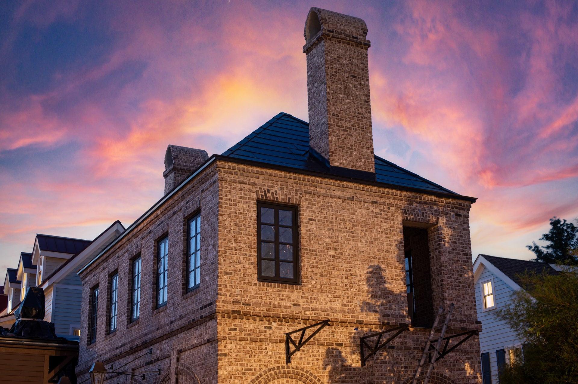 A brick house with a tall chimney stands against a colorful sunset sky.