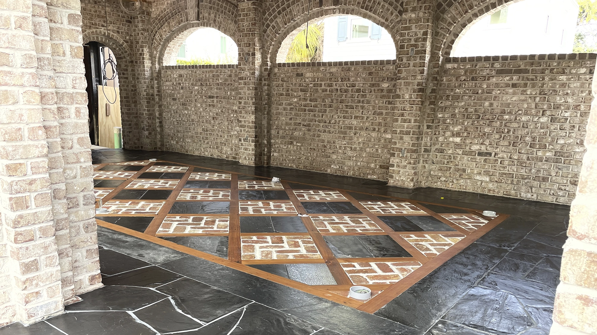 A brick hallway with arched openings and a patterned floor of bricks and tiles.