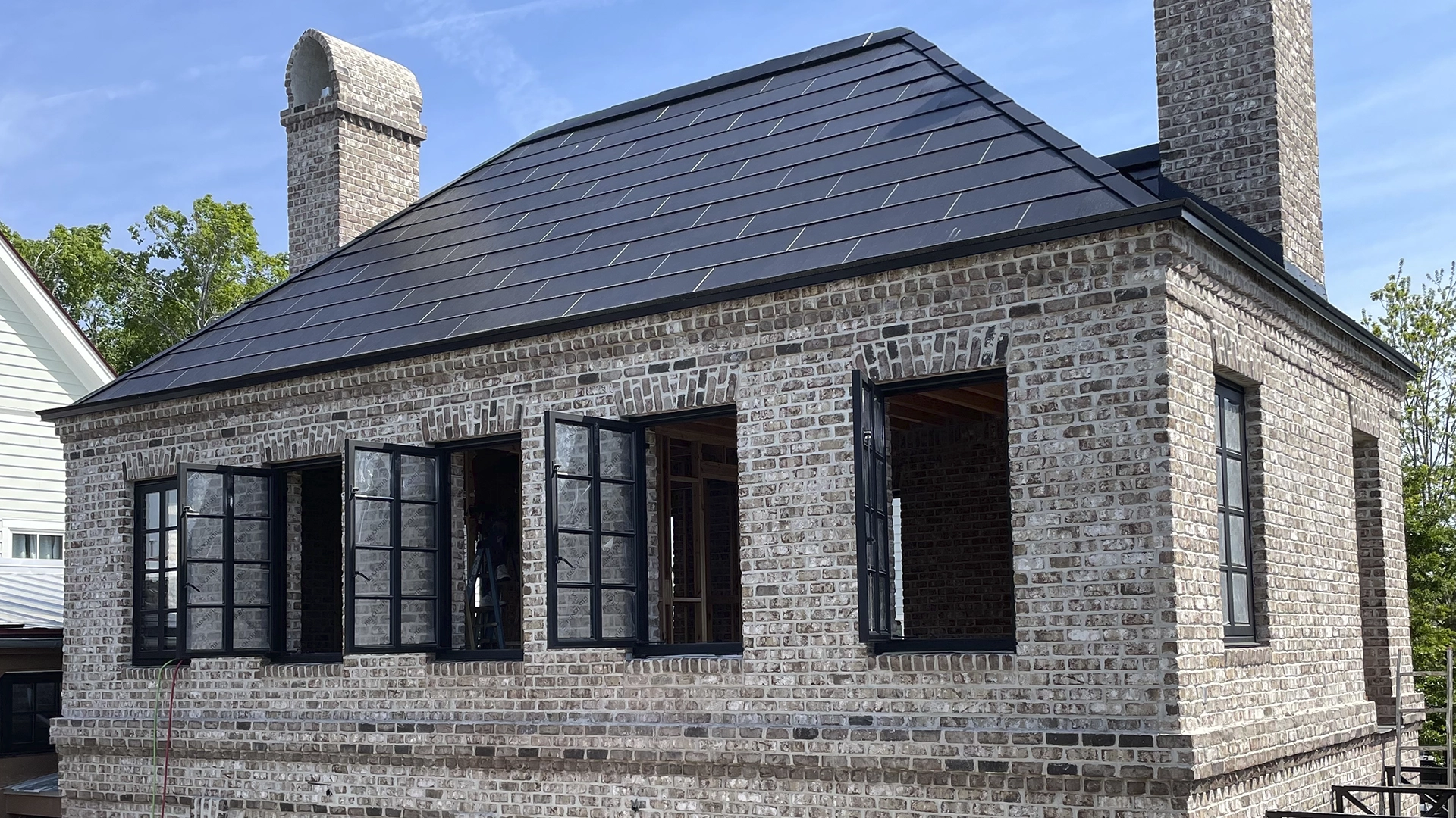 Brick building with black-framed open windows and a dark tile roof under a clear blue sky.